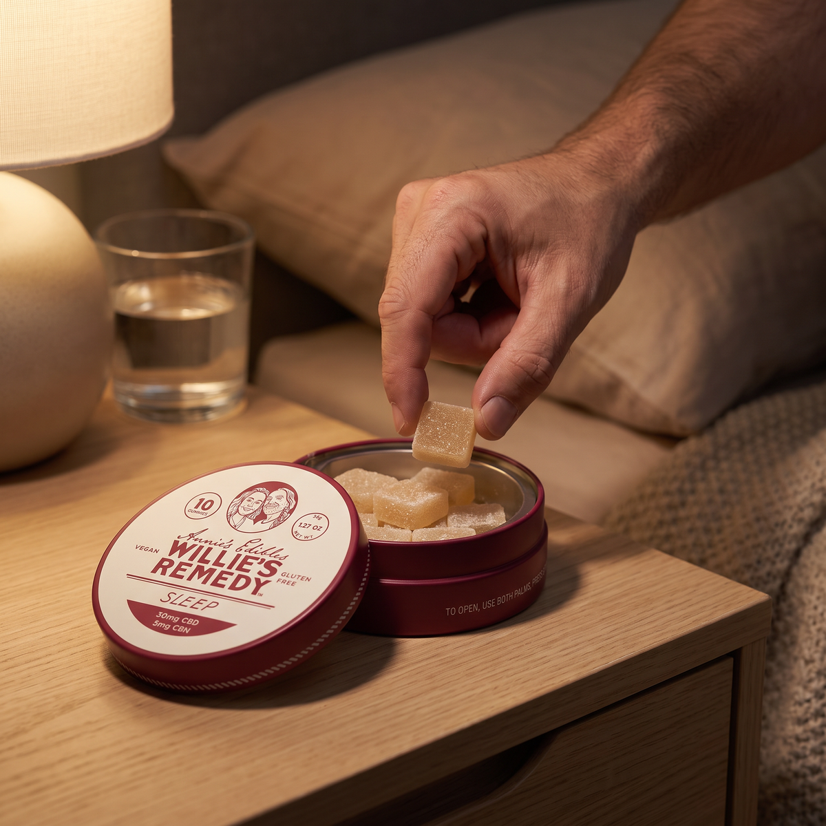Hand opening a tin of Sleep CBD gummies by a bedside lamp
